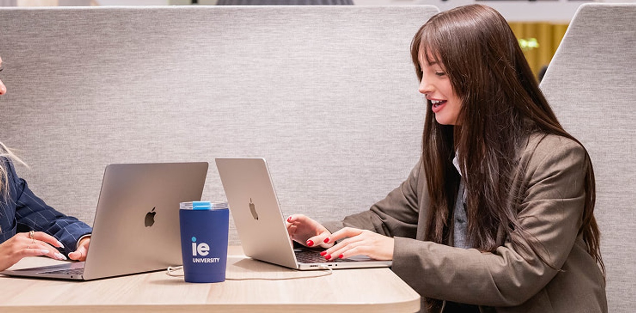 Two people are working on laptops at a table in a modern cafe.