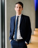 A young man in a business suit standing confidently in a modern office environment.