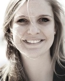 Portrait of a smiling woman with blond hair blown by the wind, standing outdoors.