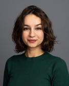 Portrait of a smiling young woman with short curly hair wearing a green sweater against a gray background.