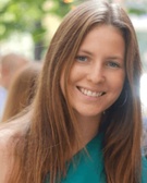 A smiling woman with long brown hair wearing a green top.