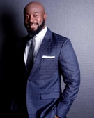 A man in a tailored suit smiling against a gray background.