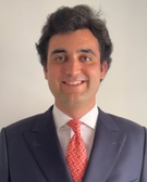 Portrait of a smiling man wearing a dark suit and a red tie.