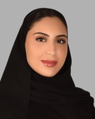 Portrait of a smiling woman wearing a black hijab against a gray background.