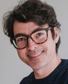 Portrait of a smiling man with curly hair wearing glasses.