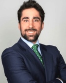 A professional portrait of a smiling man wearing a blue suit and green tie.