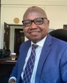 A man in a blue suit and purple tie smiling in an office setting.