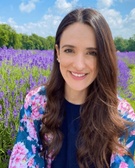 A woman smiling in a field of purple lavender under a clear blue sky.