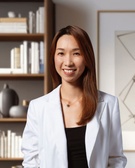 A smiling woman in a white blazer stands in front of a bookshelf.