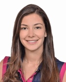 Portrait of a smiling young woman with long hair wearing a sleeveless blue and pink top against a plain background.