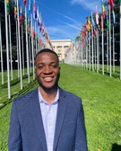 A smiling man in a suit standing in front of rows of international flags.