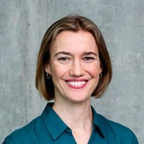 A woman with a joyful smile is posing in front of a concrete wall.