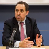 A man in a suit with a tie speaking at a podium.