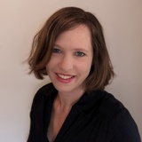 A portrait of a smiling woman with short brown hair, wearing a black blouse.