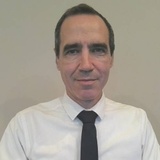 A portrait of a smiling middle-aged man wearing a white shirt and a black tie.