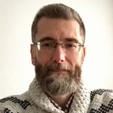 Portrait of a man with a beard and glasses wearing a knitted sweater.