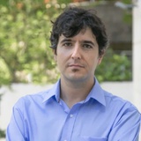 A man in a blue shirt looking at the camera with a serious expression.