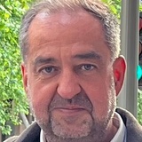 A close-up portrait of a middle-aged man with a slight smile, standing outdoors with trees in the background.