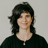 A portrait of a smiling woman with dark hair, wearing a black top and a necklace.