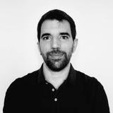 Portrait of a man with a beard wearing a black shirt against a white background.