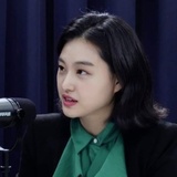A young Asian woman in a green blouse sitting in front of a microphone, probably engaged in a podcast or interview.