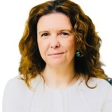 A person with curly hair wearing a white top and earrings.