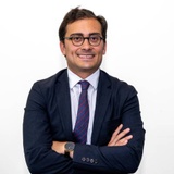 A professional man in a suit with glasses smiling at the camera, arms crossed.