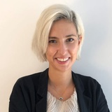 A professional portrait of a smiling woman with short blonde hair, wearing a black blazer over a white blouse.