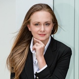 A professional woman in a suit with her hand on her chin, posing thoughtfully.