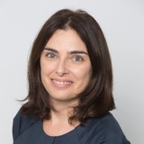Portrait of a smiling woman with shoulder-length dark hair wearing a dark blue top.