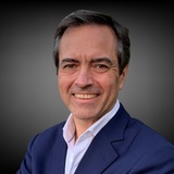 A portrait of a smiling man wearing a blue suit and pink shirt.