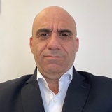 A portrait of a bald man wearing a suit and a white shirt, looking directly at the camera with a serious expression.