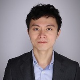 A professional headshot of a smiling Asian man wearing a suit and light blue shirt.
