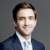 A professional portrait of a smiling man in a suit and tie.