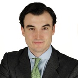A professional portrait of a man in a dark suit and green tie, smiling at the camera.