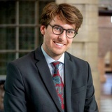 A smiling man in a suit and tie poses for the photo.