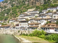 A picturesque view of a town with traditional white houses built on the slope of a lush hill beside a river.