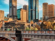 A scenic view of a city skyline with modern skyscrapers and a bridge over a river, captured during the daytime.