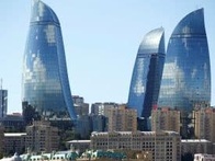 A cityscape showing three modern glass skyscrapers towering over urban buildings under a clear sky.