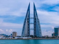 Modern twin skyscrapers standing tall beside a tranquil city waterfront under a partly cloudy sky.