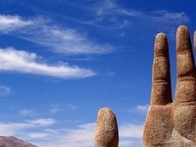 A large sculpture of a hand partially buried in a desert with a clear blue sky in the background.