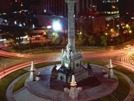 A night view of the Angel of Independence monument with illuminated busy traffic trails in Mexico City.