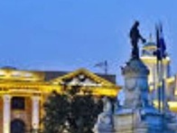 A statue stands prominently in front of a historic building illuminated at twilight.