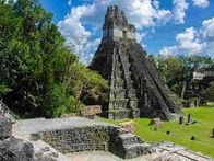 A photo of an ancient Mayan pyramid surrounded by lush greenery under a clear blue sky.