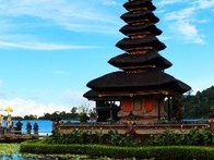 A multi-tiered temple by a lake with blooming water lilies under a blue sky.