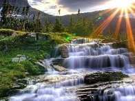 A breathtaking view of cascading waterfalls with the sun setting behind mountainous terrain.