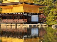 A golden pavilion reflecting in a calm water body surrounded by trees under a clear sky.