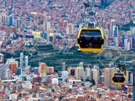 Aerial view of a city with a cable car system traversing above densely packed buildings and high-rises under a clear sky.