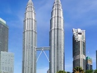 A view of the Petronas Twin Towers with a clear blue sky, surrounded by lush greenery and a reflective pond.