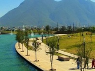 A scenic view of a riverwalk with young trees lining the path, overlooking a majestic mountain in the background.